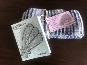 A handknit scarf ready for donation is shown with the first edition of the KnitServe ‘zine.
