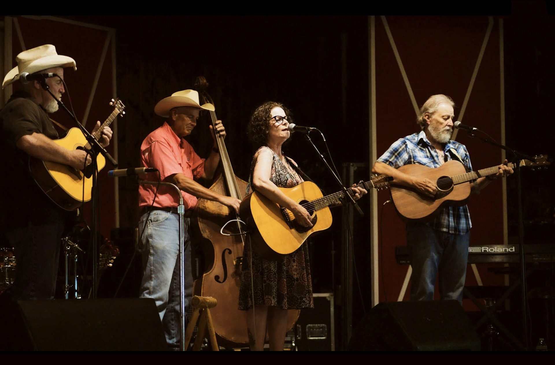 Gypsy Twang band performing live at Arcadia Round Barn, featuring members playing acoustic guitars, upright bass, and mandolin under stage lights.